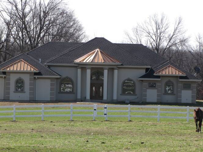 Large stucco residence with copper-roofed bays behind a white fence