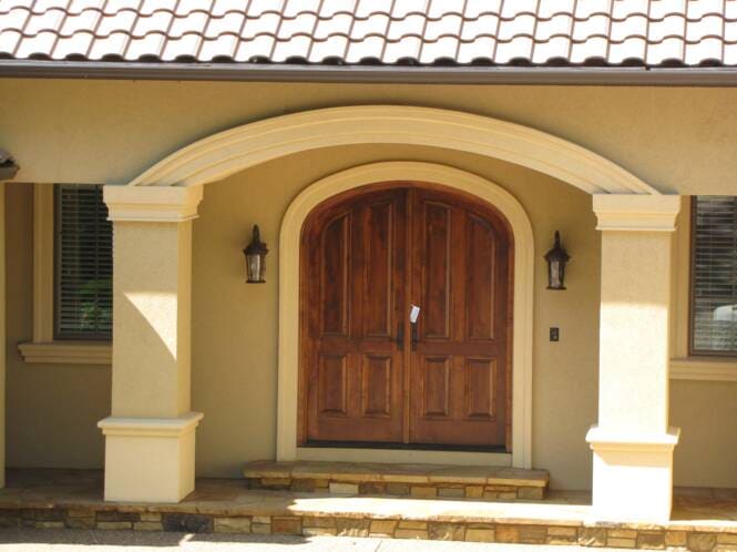 Arched wood entry between stucco columns under a tile roof