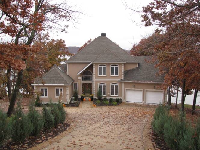 Two-story home in stucco and stone among mature trees